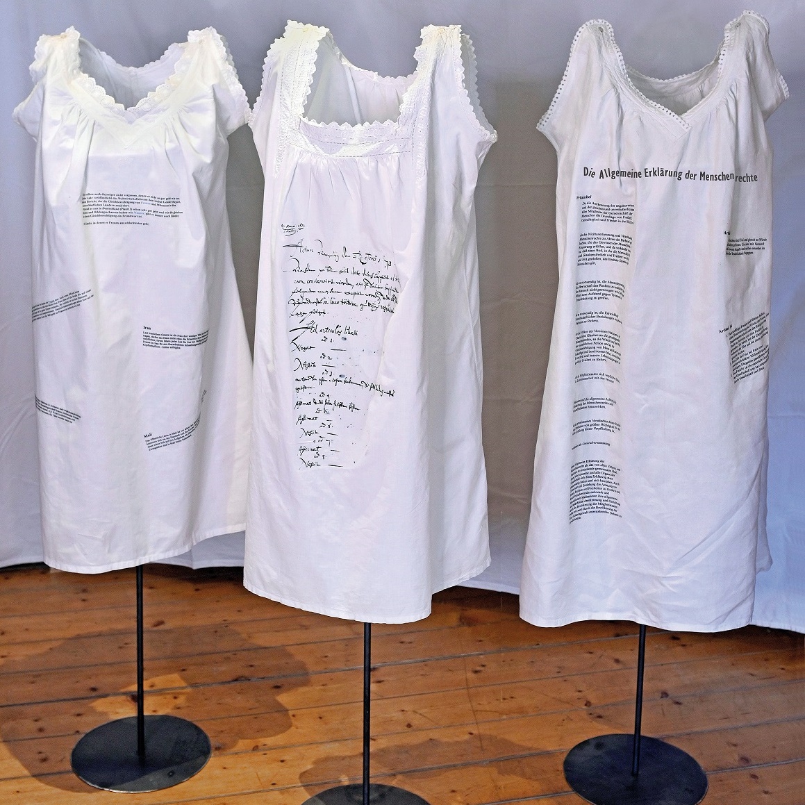 Drei Kleiderständerm, auf denen weiße Nachthemden hängen, die beschriftet sind.