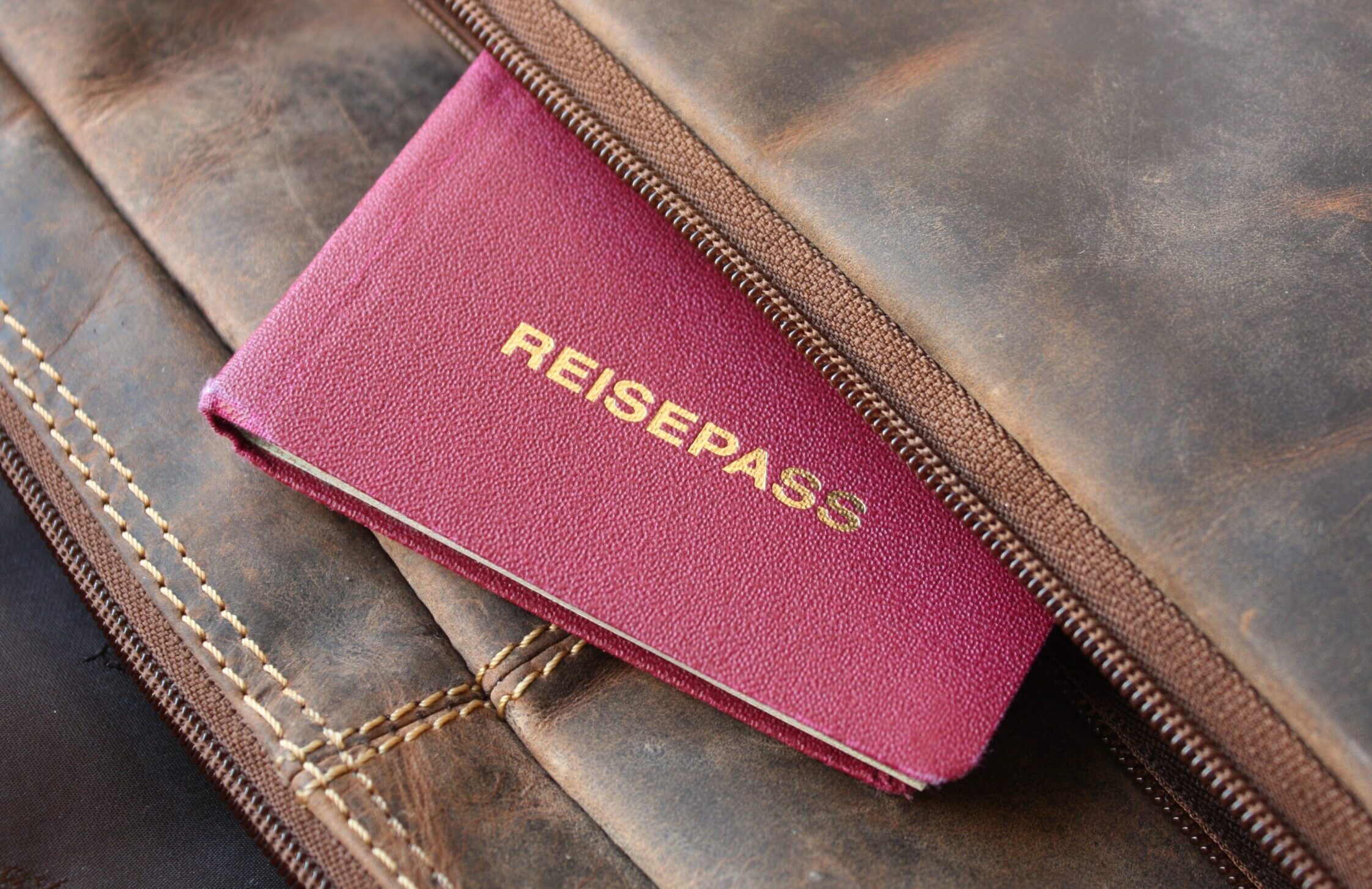 Ein Reisepass guckt aus einer braunen Ledertasche heraus. Das Wort "Reisepass" ist zu lesen.