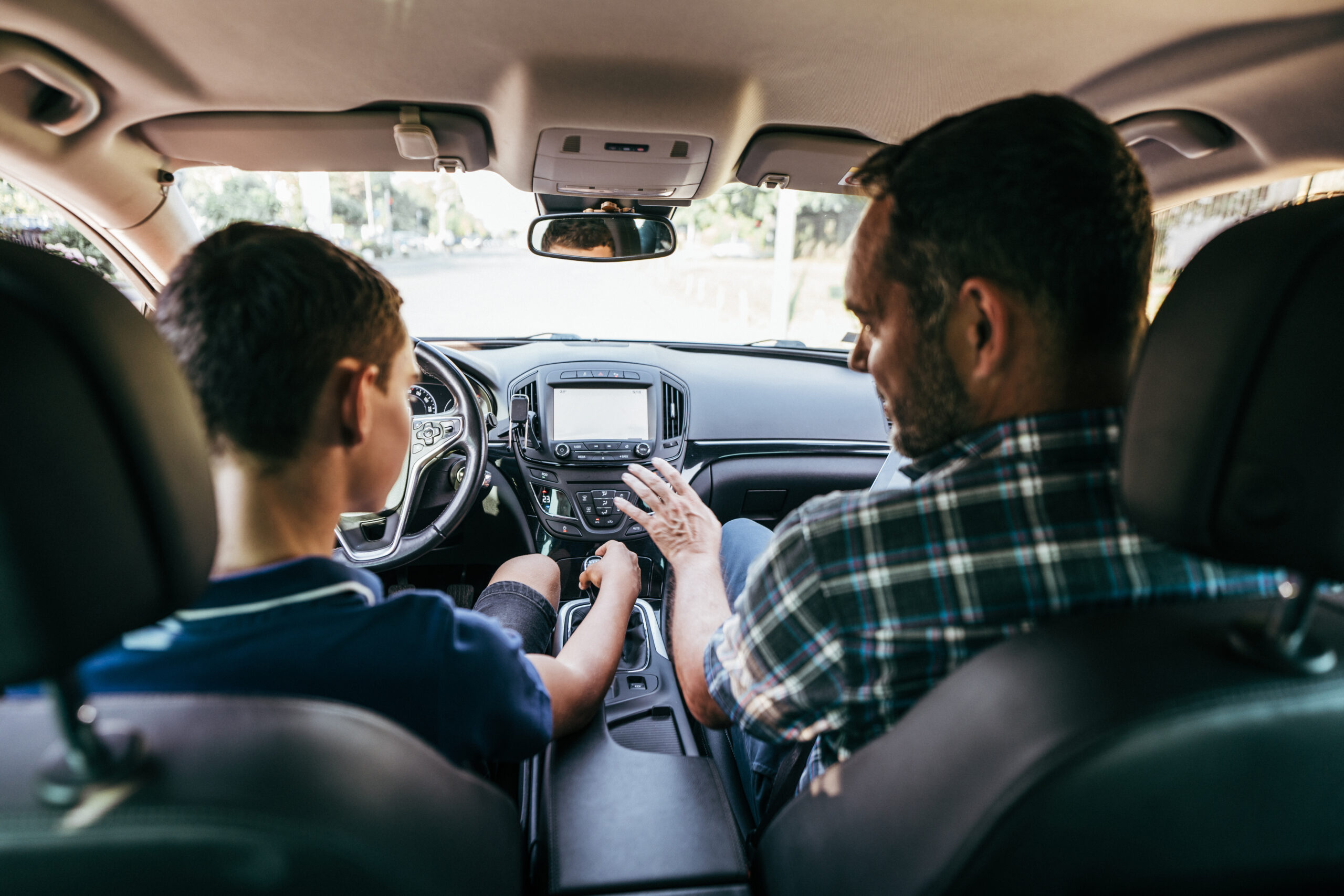 Vater und Sohn sitzen im Auto, der Jugendliche auf dem Fahrersitz